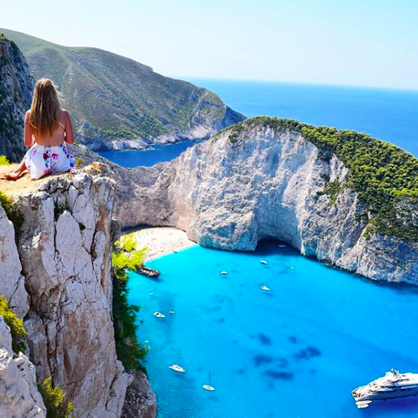 Girl sitting on cliffside at Navagio Beach in Zakinthos Europe