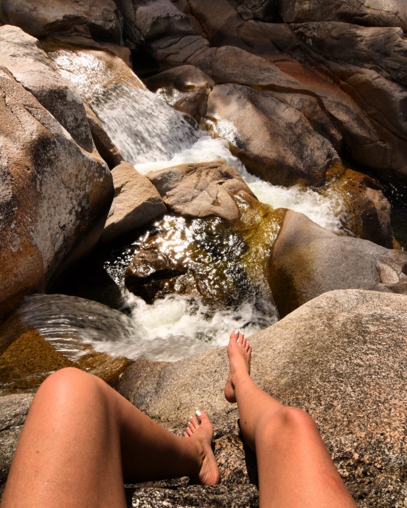 Girls legs hanging out over rock over water below at Behana Gorge in Cairns