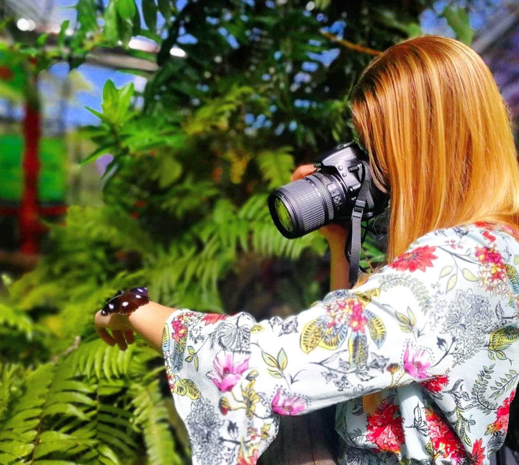 Girl taking a photo of a butterfly resting on her hand