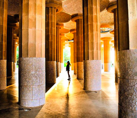 Girl standing in sunlight in columns at Park Guell