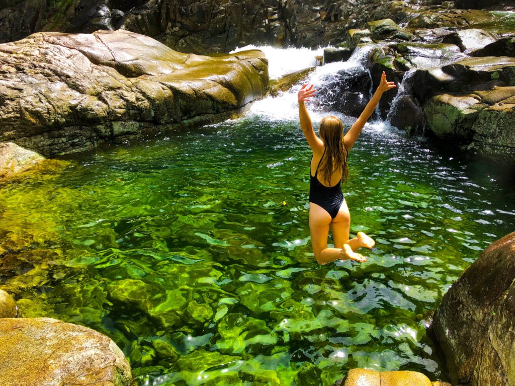 Girl jumping into green rock pool at Behana Gorge in Cairns