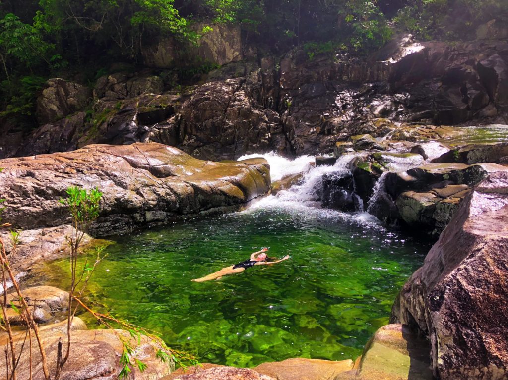Girl floating in clear green rock pool in Behana Gorge in Cairns