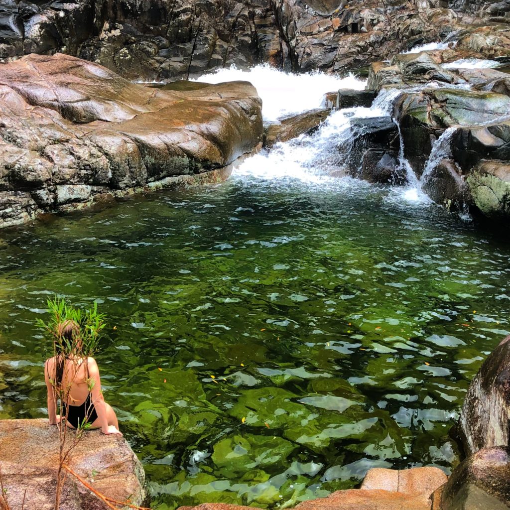girl sitting next to clear green rock pool 