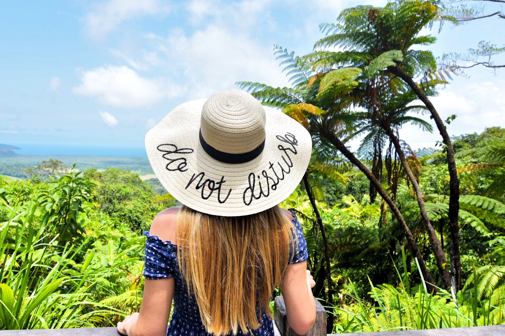 Girl standing in front of rainforest lookout with sunhat that says Do Not Disturb