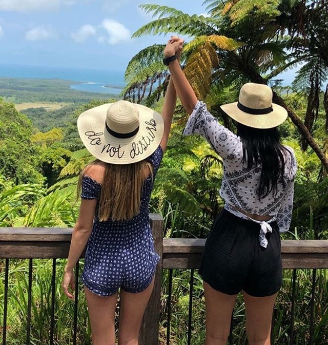 Two girls in sun hats holding hands overlooking rainforest lookout