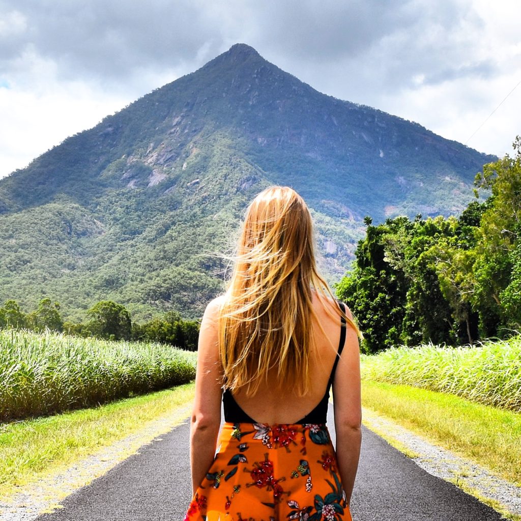 Girl standing on road looking up at pyramid shaped mountain