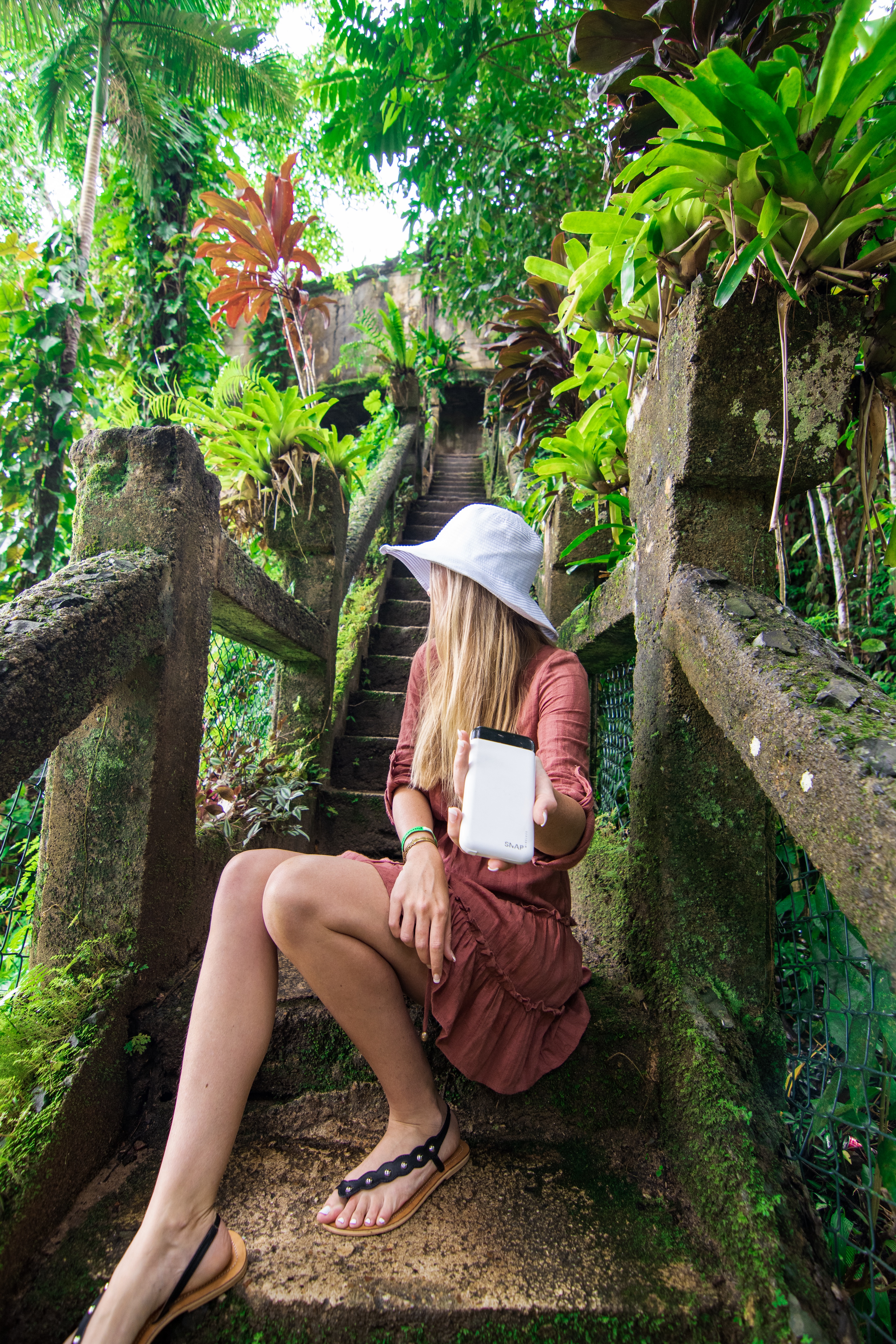 Girl holding Snap Wireless battery pack charger sitting on staircase in the rainforest at Paronella Park