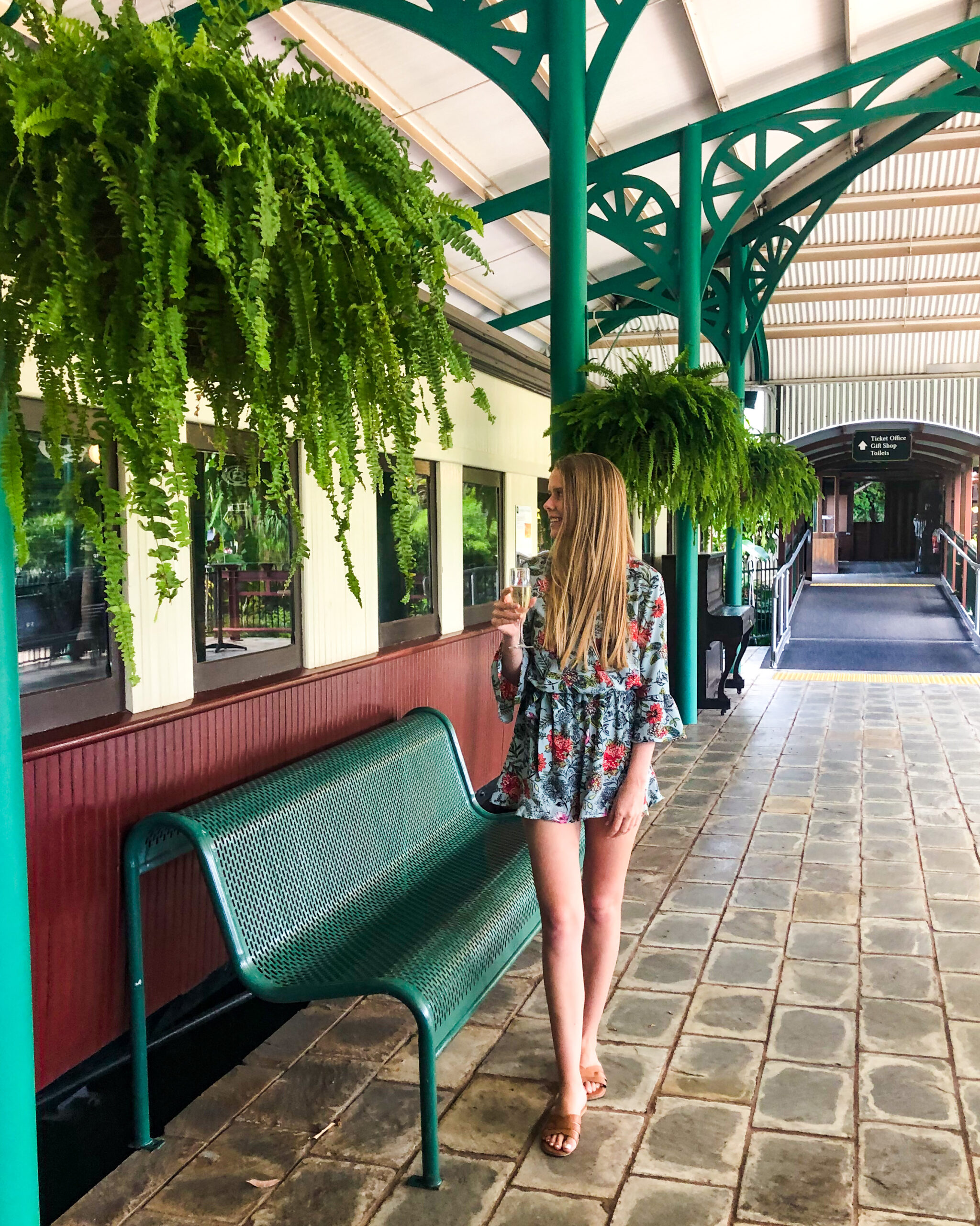 Girl standing holding champagne glass in front of train carriage at train station at the High Tea Trolley